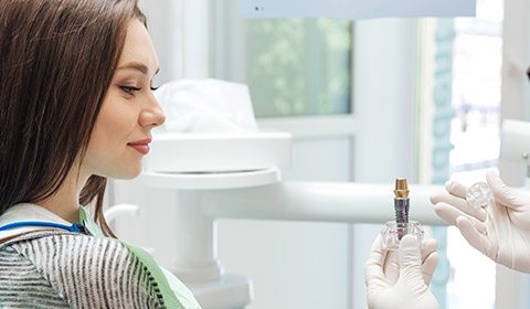 Woman in dental chair looking at implant model