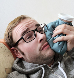 A man lying on the couch with a cold compress on his cheek