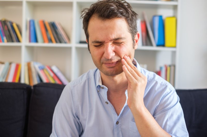 Man with gum disease on couch rubbing jaw