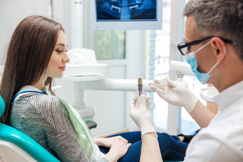 Dentist with glasses showing dental implant to female patient